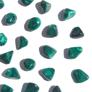 Malaquite rolada natural de tamanho pequeno em grupo sobre fundo branco, cristal para proteção, cura e transformação.